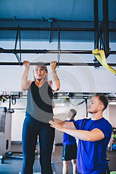 Woman doing pull-ups and a man securing her.