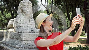 Woman doing selfie with sphinx statue on mobile phone in slow motion in Villa Borghese on sunny day