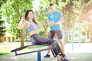Woman doing sit ups outdoor with her trainer.