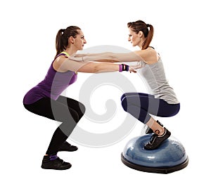 Woman doing squats on a bosu ball, helped by the peronal trainer