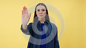 Woman doing stop sign with palm while looking seriously at camera indoors