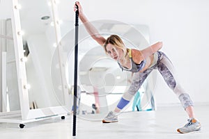 Woman doing stretching exercise for hamstrings and back leaning forward holding barbell in one hand