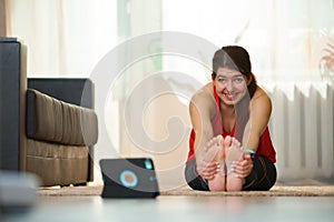 Woman is doing stretching, practicing yoga exercises at home using video tutorials.