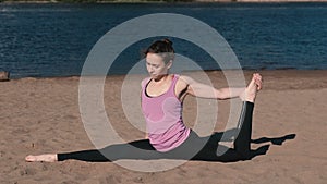 Woman doing stretching sitting on twine in the sandy beach at sunset.