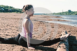 Woman doing stretching sitting on twine in the sandy beach at sunset.