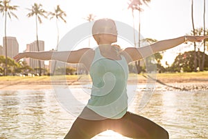 Woman doing SUP yoga in Waikiki at sunrise warrior pose