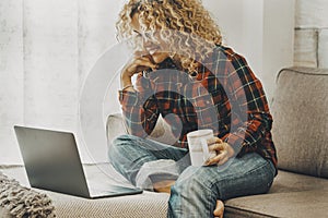 Woman doing video call conference comfortably sitting on the sofa at home in technology leisure activity. Female using computer on
