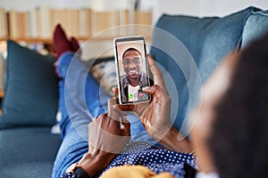 Woman doing video call with her black boyfriend lying on sofa