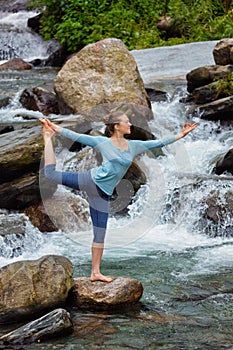 Woman doing yoga asana Natarajasana outdoors at waterfall