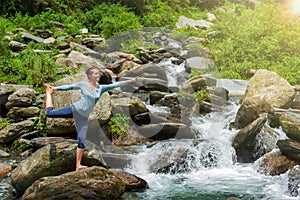 Woman doing yoga asana Natarajasana outdoors at waterfall