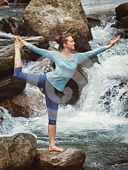 Woman doing yoga asana Natarajasana outdoors at waterfall