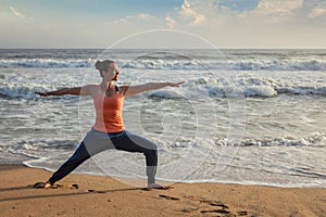 Woman doing yoga asana Virabhadrasana 1 Warrior Pose on beach on