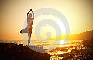 Woman doing yoga on the beach at sunset