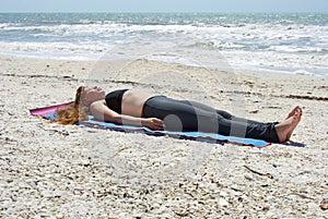 Woman doing yoga corpse pose on beach