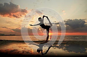woman doing yoga dancer pose on beach over sunset