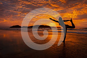 Woman doing Yoga dancer pose at sunrise on the beach