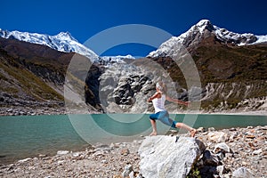 Woman is doing yoga excercises near big lake on the Manaslu circuit trak in Nepala