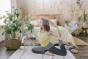 Woman doing yoga exercise in her light stylish bedroom at home. Morning workout in bedroom. Healthy and sport lifestyle.