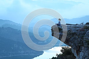 Woman doing yoga exercise in the top of a cliff on blue