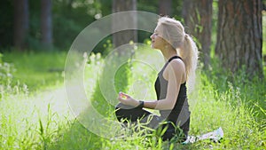 Woman doing yoga outside in the park. She sitting on lotus pose.