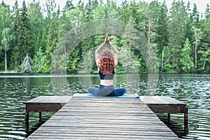 woman doing yoga on the pier of a beautiful lake.  Concept of healthy life and natural balance