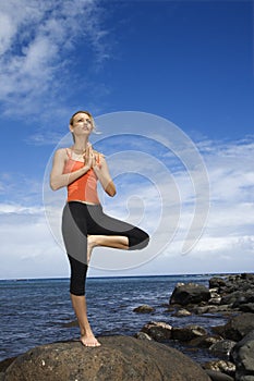 Woman doing yoga on rocky shore.