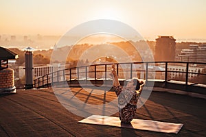 Woman doing yoga on the roof of a skyscraper in big city.