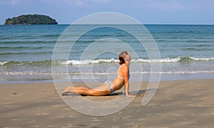 Woman doing yoga on sand beach. Tropical seaside vacation activity. Young girl in asana posture.