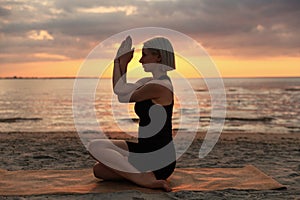 woman doing yoga seated eagle pose on beach