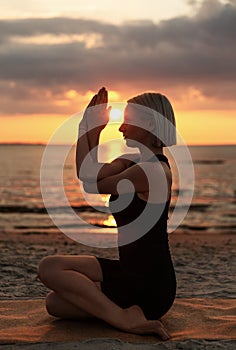 woman doing yoga seated eagle pose on beach