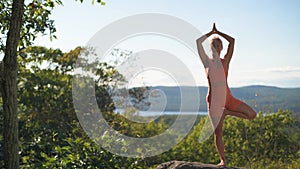 Woman is doing yoga training on the top of a mountain at sunset. Meditation and harmony in tree pose