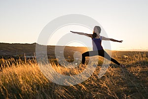 Woman doing yoga warrior II pose during sunset