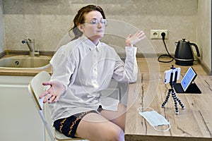 A woman in doubt shrugs her hands at a remote work in the quarantine of the coronavirus. Girl sitting sad in the kitchen in front