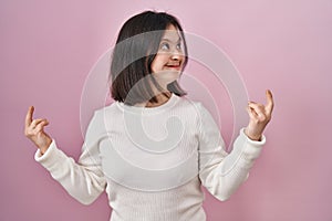 Woman with down syndrome standing over pink background showing middle finger doing fuck you bad expression, provocation and rude