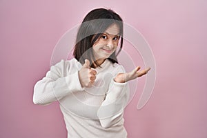 Woman with down syndrome standing over pink background showing palm hand and doing ok gesture with thumbs up, smiling happy and