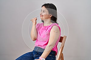Woman with down syndrome wearing band aid for vaccine injection pointing thumb up to the side smiling happy with open mouth
