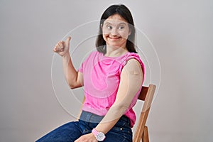 Woman with down syndrome wearing band aid for vaccine injection smiling happy and positive, thumb up doing excellent and approval