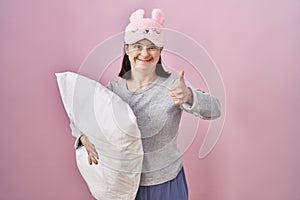 Woman with down syndrome wearing sleeping mask hugging pillow doing happy thumbs up gesture with hand