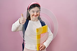 Woman with down syndrome wearing student backpack and holding books doing happy thumbs up gesture with hand