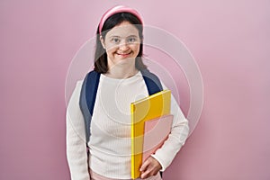 Woman with down syndrome wearing student backpack and holding books with a happy and cool smile on face