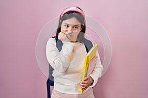 Woman with down syndrome wearing student backpack and holding books looking stressed and nervous with hands on mouth biting nails