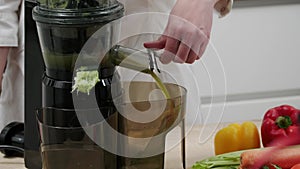 A woman drains vegetable juice from a juicer. Healthy detox vegetarian diet with cold pressed plant extractor for bread and