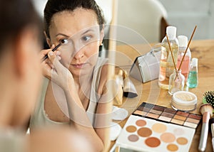 Woman drawing eyeliner wing in front of home vanity mirror