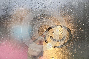 Woman drawing happy face on foggy window at rainy weather, closeup