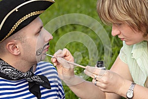 Woman drawing whiskers and beard on man's face