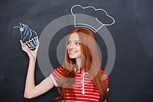 Woman in drawn chef hat holding drawing cupcake over blackboard