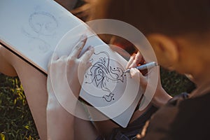 Woman draws letters in the park. Outline hand lettering in a sketchbook