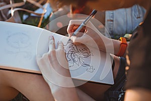 Woman draws letters in the park. Outline hand lettering in a sketchbook