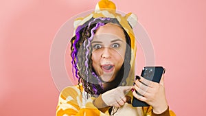 Woman with dreadlocks uses a smartphone and is very and sincerely happy about the online victory. A female in kigurumi