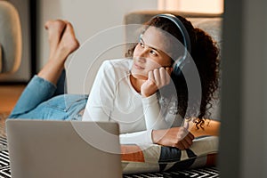 woman dreaming and listening to music. Young woman listening to music through headphones on her laptop. Girl lying on